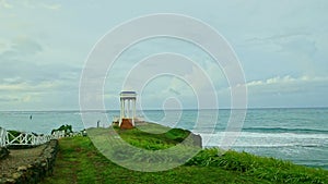 slowly panorama of white gazebo on green hill against blue ocean with strong waves