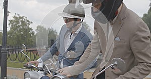 Slowmo of confident men and woman sitting on scooters outdoors under rain. Portrait of Caucasian bikers in formalwear