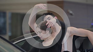 Slowmo dance of young caucasian ballet dancers in car showroom. Camera following moves of man and woman dancing in auto