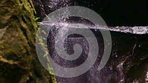 slowmo of a dark rocky jungle waterfall with rocks in the foreground with green plants