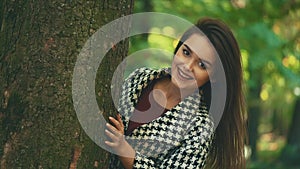 Slowmo. Happy smiling caucasian girl is showing up from tree caudex, isolated, on blurred park background. Close up