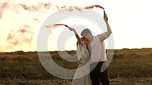 Slowmo of man and woman who are standing in field and waving smoke bombs on gender reveal party