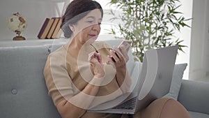 Slowmo of mature Caucasian woman tapping smartphone screen and smiling. Positive senior businesswoman surfing Internet