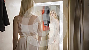 Slowmo of young elegant caucasian woman looking at reflection in dressing room. Confident rich lady trying on dress in