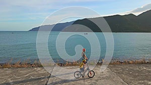 Slowmotion aerial shot. Woman and her son ride kick scooterand bicycle by the sea during sunset