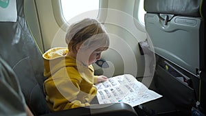 Slowmotion shot of a boy in yellow jacket on board of an airplane reading a safety instruction