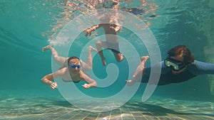 Slowmotion underwater shot of a happy family diving in a swimming pool. Healthy lifestyle, active parents