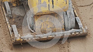 Slowmotion working petrol yellow plate compactor thickening sand surface