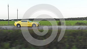 A slowmotion of a yellow sports car moving on the country road