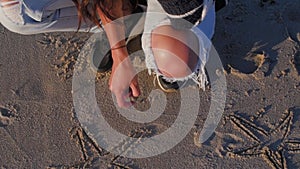 Slowmotion of young woman writing the word of Love on the sand sea beach. Girl draw on the sandy near waves in warm