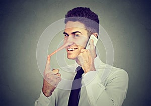 Sly young man with long nose talking on mobile phone on gray wall background. Liar concept.