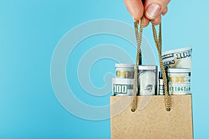 A small aid Bag made of paper in an outstretched hand with US dollars on a blue background. Packaging template layout with space