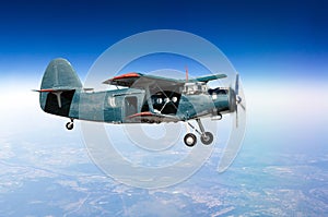 Small aircraft turboprop biplane at high altitude in the sky above the ground with an open door.