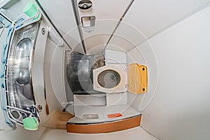 Small aircraftspacecraft lavatory with a sink, waste bin, and control panel-like object Subdued color scheme, muted greys, whites photo