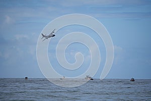 Small airplane soaring over a white boat sailing in the sparkling blue ocean