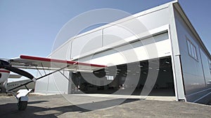 Small airplanes outside hangar. Door is opening. Visible part of a small aircraft photo