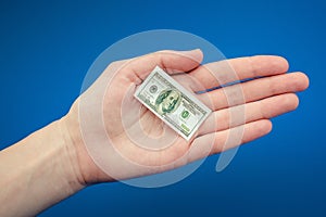 Small American dollar bill in hand on a blue background