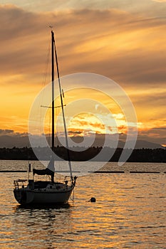 a small anchored sail boat floating at golden hour