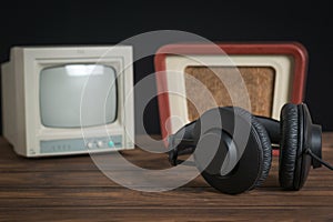 A small antique TV, radio and headphones on a wooden table.