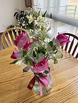 Small arrangement of pink roses with white flowers in a vase with pink bow