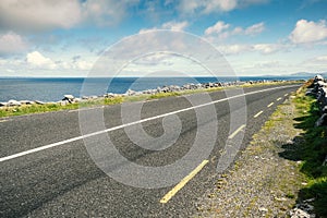 Small asphalt road by Atlantic ocean, Burren National geo park, Ireland. Nobody, Warm sunny day. Beautiful cloudy blue sky. Part