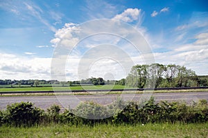 Small asphalt road with beautiful country landscape in the background. Blue cloudy sky over green fields. Travel concept. Nature