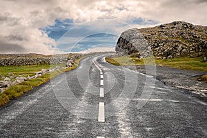 Small asphalt road on West coast of Ireland, part of Wild Atlantic Way route. Beautiful cloudy sky in the background, Rough stone photo