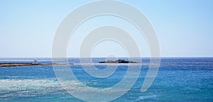 A small atoll in the blue sea with blue sky in the background