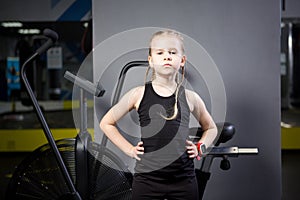 Small attractive caucasian child using exercise bike in the gym. Fitness. A little athlete using an air bike for a cardio workout