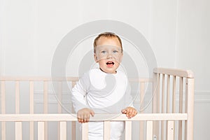 Small baby boy 2 years old in the crib looking at the camera in the bright children`s room, the child after sleeping