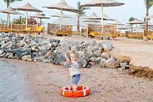 Small baby boy with adorable face with lifebelt on beach
