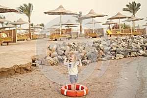 Small baby boy with happy face with lifebelt on beach