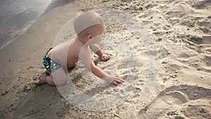 Small baby boy playing in the wet sand on the beach He learns to crawl