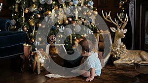 Small baby girl crawling near the Christmas tree with gifts