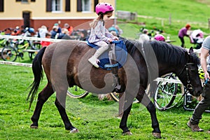 Small baby girl in pink helmet ride pony