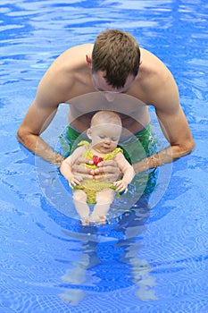 Small baby girl is swimming in the pool with daddy