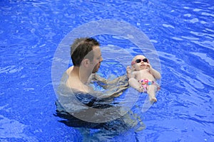 Small baby girl is swimming in the pool with daddy