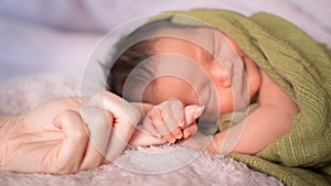 Small baby infant hand holding mother woman finger when sleeping on soft bed.
