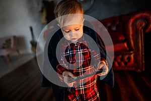 Small baby is standing and holding tablet in hands. He is looking at it. Child is concentrated