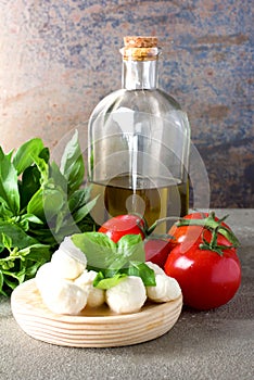 Small balls of mozzarella with basil leaves, tomato and olive oil on rustic background