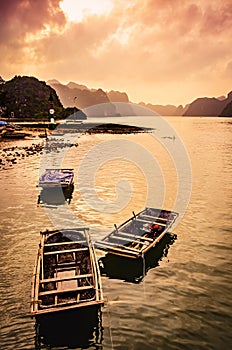 Small bamboo fishing boats in the sea in Ha Long Bay with sunset over the stunning karst stone mountain scenery. Cat Ba Island,