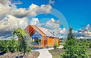 Small barnhouse on a plot with green trees under a cloudy sky. Modern small housing