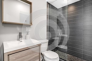 A small bathroom with a light wood vanity and a grey tiled shower.
