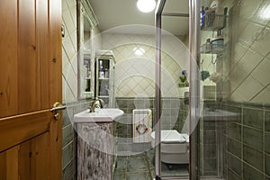 Small bathroom with multi-toned green tiles, walk-in shower with glass partitions, stripped wood-framed mirror, and matching