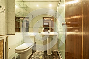 Small bathroom with pedestal porcelain sink, large mirror on the wall and old tiles