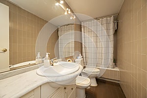 Small bathroom with porcelain sink with white chest of drawers, long mirror without frame with sconces and bathtub with white