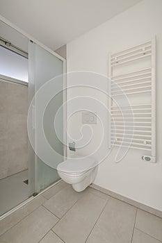 Small bathroom with a radiator, toilet bowl and an open shower. There is also a small window