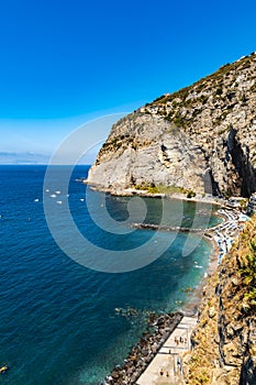 Small beach full of colorful sunbeds and umbrellas next to high cliff