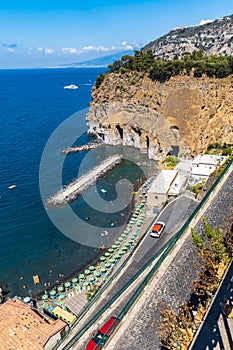 Small beach full of colorful sunbeds and umbrellas next to high cliff
