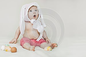 small beautiful baby sitter in rabbit hat. girl celebrates Easter and found painted eggs